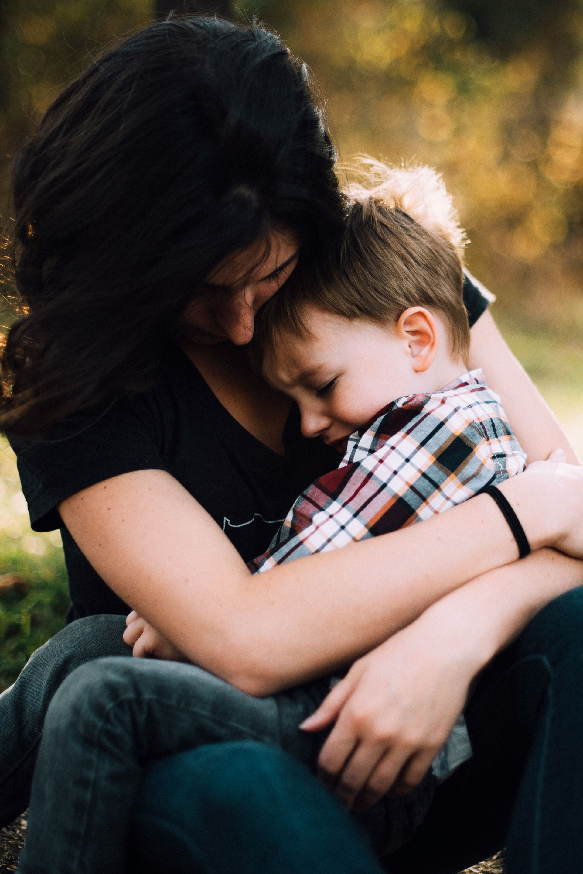 a child in a plaid shirt, hugging a woman in a black t-shirt